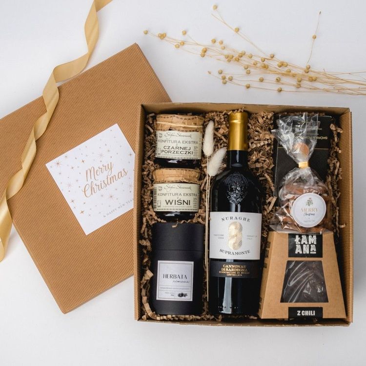 Brązowe pudełko kraft z czerwonym winem, herbatą zimową, konfiturami wiśni i porzeczki, czekoladą z chili oraz piernikami świątecznymi