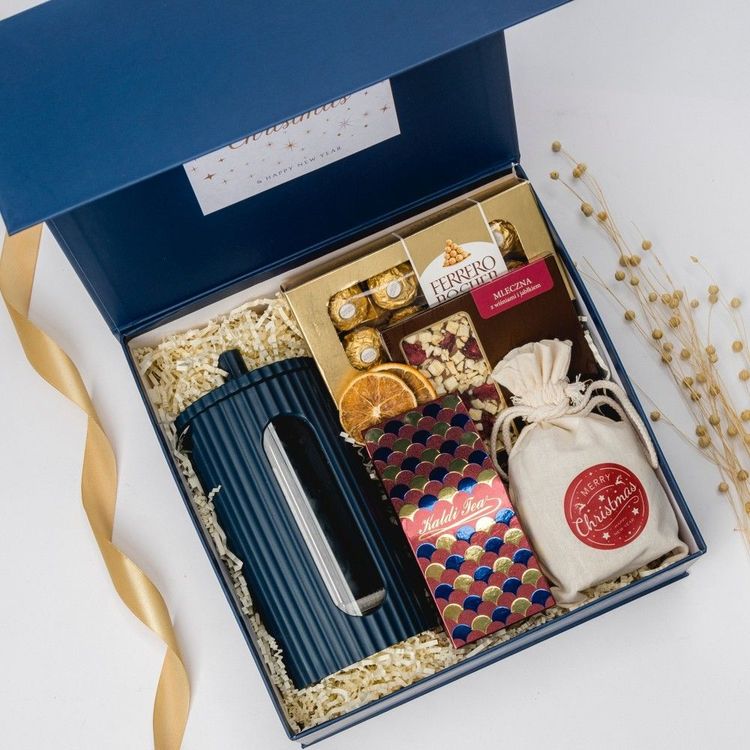 Niebieskie prostokątne pudełko z magnesem z herbatą, czekoladą Ferrero Rocher, piernikami i wstążką