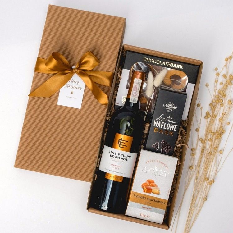 Brązowe pudełko kraft ze wstążką, czerwonym winem Merlot, czekoladą i wafelkami w świątecznej dekoracji