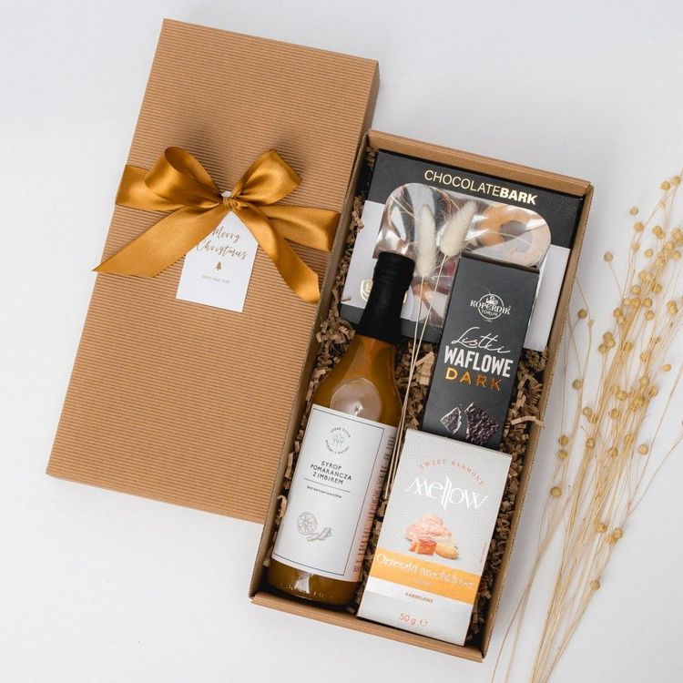 Świąteczny zestaw w brązowym pudełku kraft z butelką syropu pomarańczowego z imbirem, wafelkami, czekoladą i orzeszkami