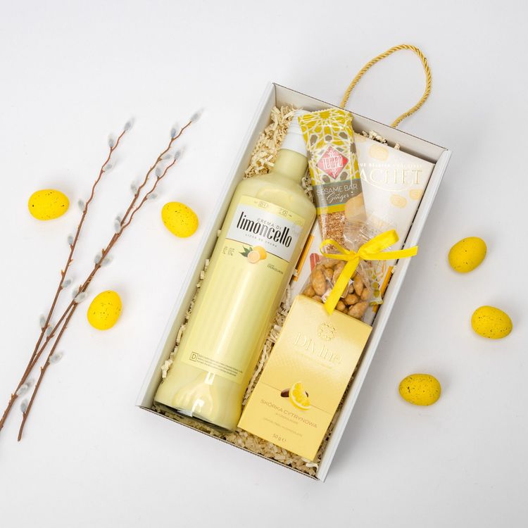 Białe prostokątne pudełko z uchwytami sznurkowymi i wstążką zawierające limoncello i czekoladki