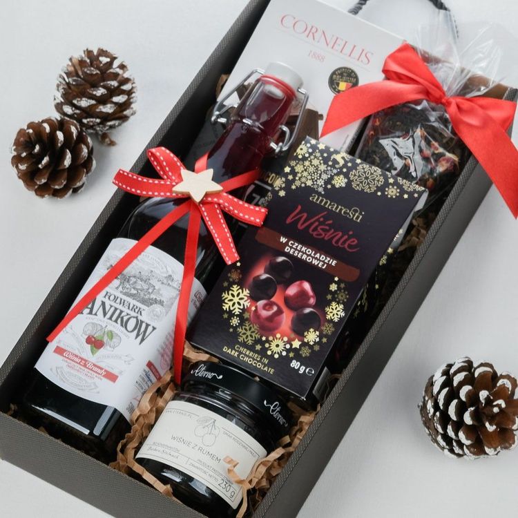Szare pudełko z uchwytami ze świąteczną wstążką i szyszką zawierające wiśnię z brandy, czekoladę i herbatę