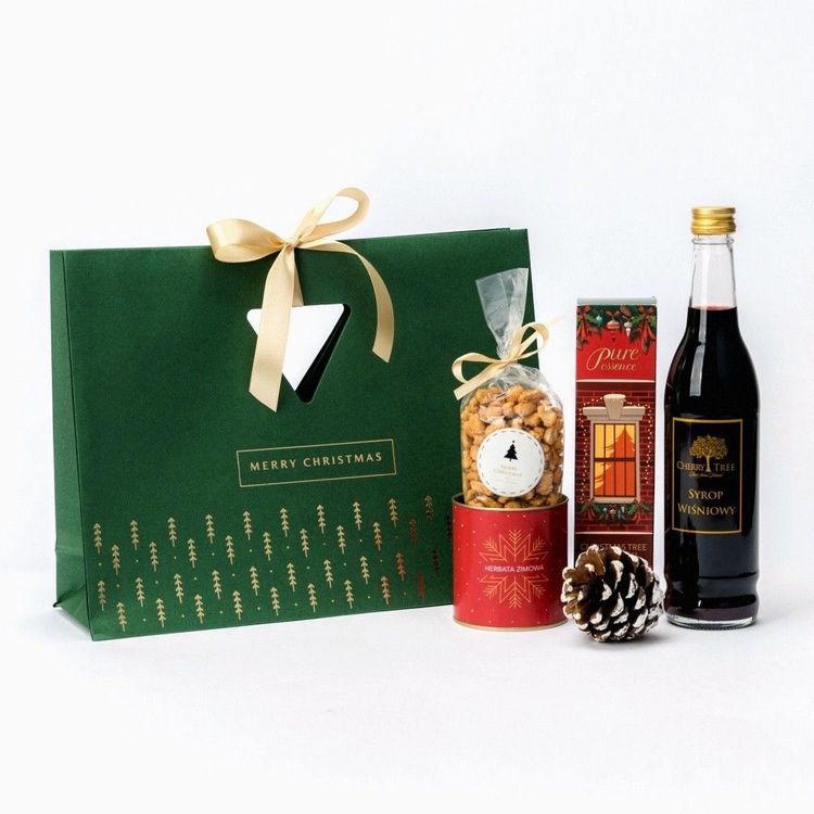 Świąteczna zielona torba papierowa z trójkątnym okienkiem, wstążką i szyszką z orzeszkami, herbatą, dyfuzorem i syropem