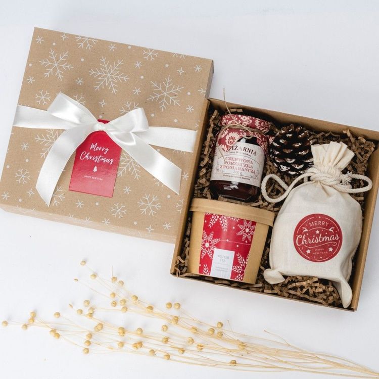 Świąteczne kwadratowe pudełko kraft ze śnieżynkami, białą wstążką i zawartością herbaty, ciastek oraz słoika